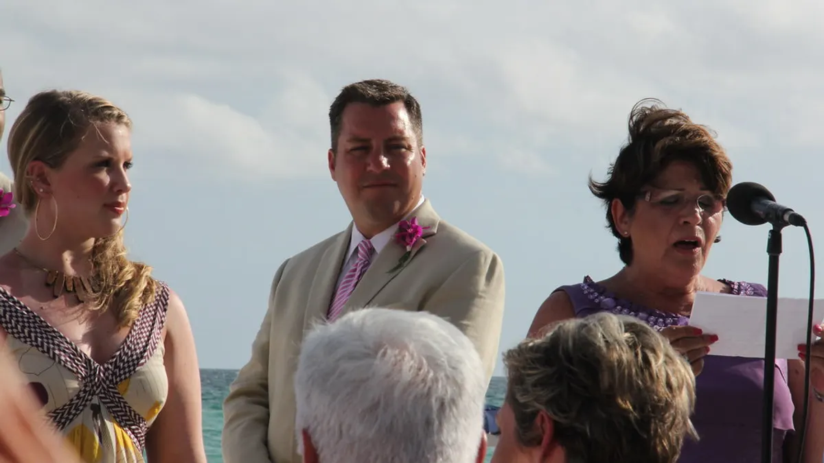 Een vrouw leest aan de microfoon een tekst voor tijdens een trouwceremonie op het strand