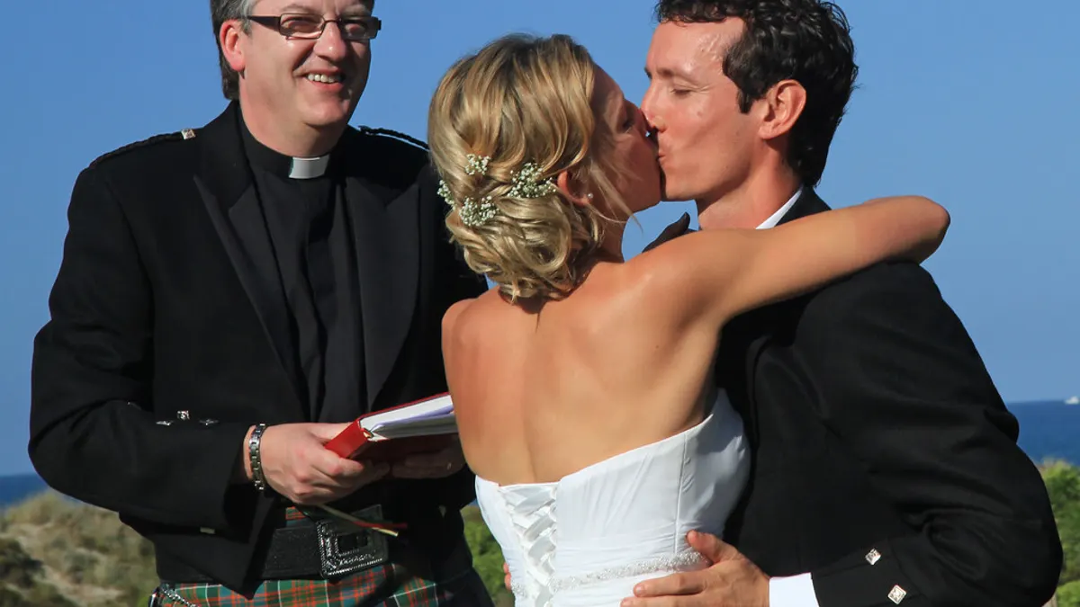 Het bruidspaar kust naast de voorganger in kilt tijdens een buitenceremonie