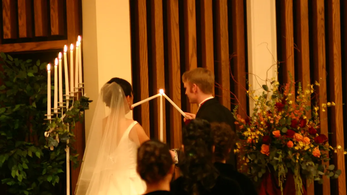 Een bruidspaar steekt samen een eenheidskaars aan tijdens de ceremonie, met familie op de voorste rij