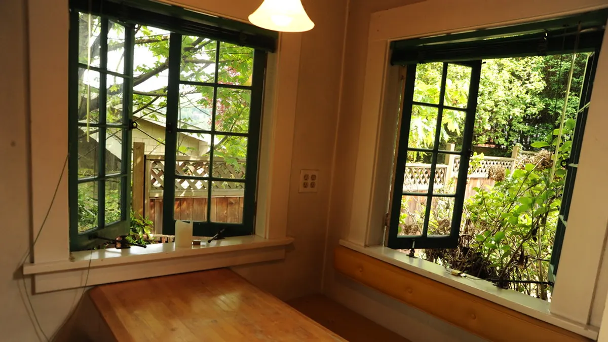 Een lege eethoek met houten tafel en open ramen naar de tuin in een huis dat te koop staat