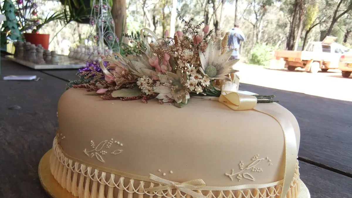 Crèmekleurige bruidstaart met gedroogde bloemen en een satijnen lint op een houten tafel buiten