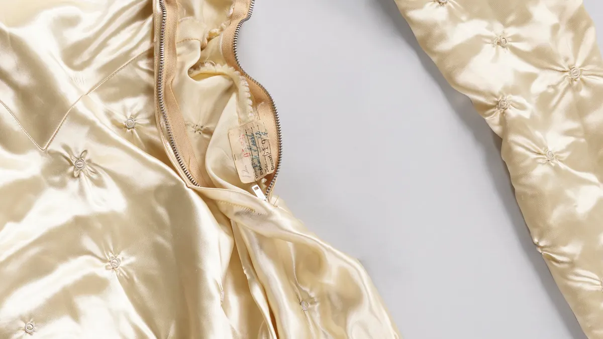 Detail van een roomkleurige satijnen trouwjurk met een open rits en kleine sierstiksels op de stof