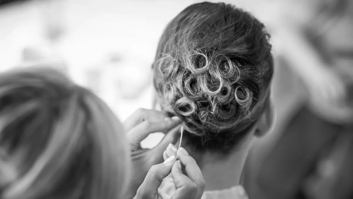 Kapster steekt het haar van een bruid op in een lage knot met krullen, zodat haar nek vrij blijft