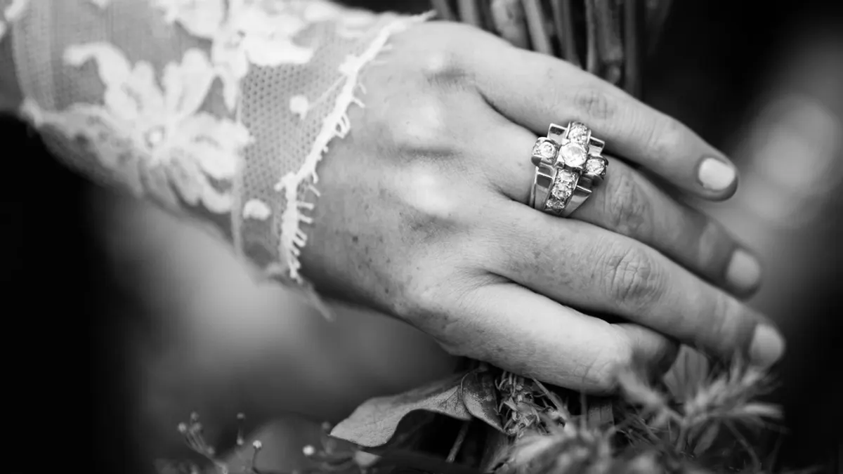 Zwart-witte close-up van de hand van een bruid met een kanten mouw tot op de pols en een fonkelende ring