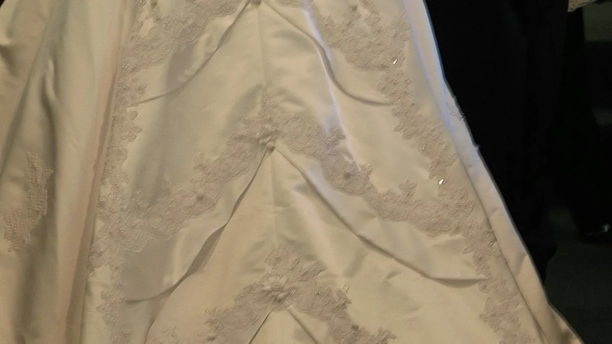 Close-up van een satijnen trouwjurk met kantapplicaties en drapering op de rok