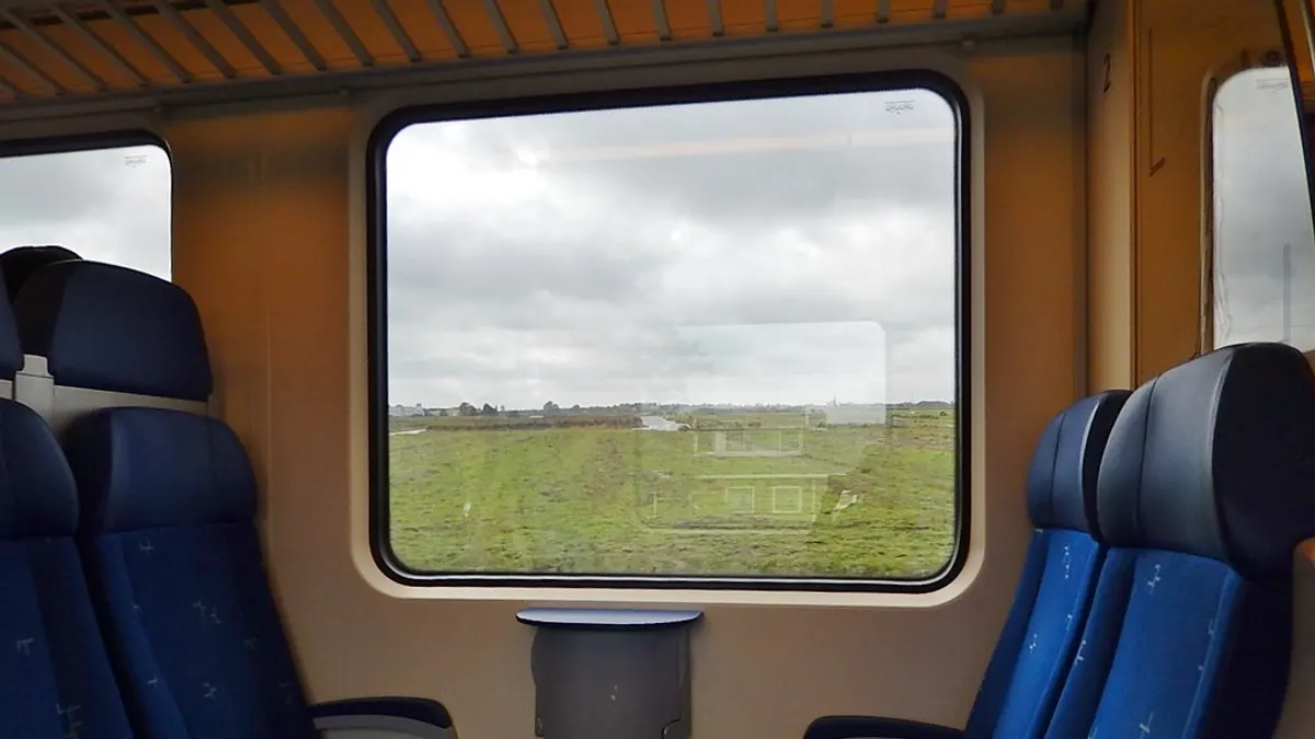 Lege treincoupé met blauwe stoelen en door het raam een groene polder