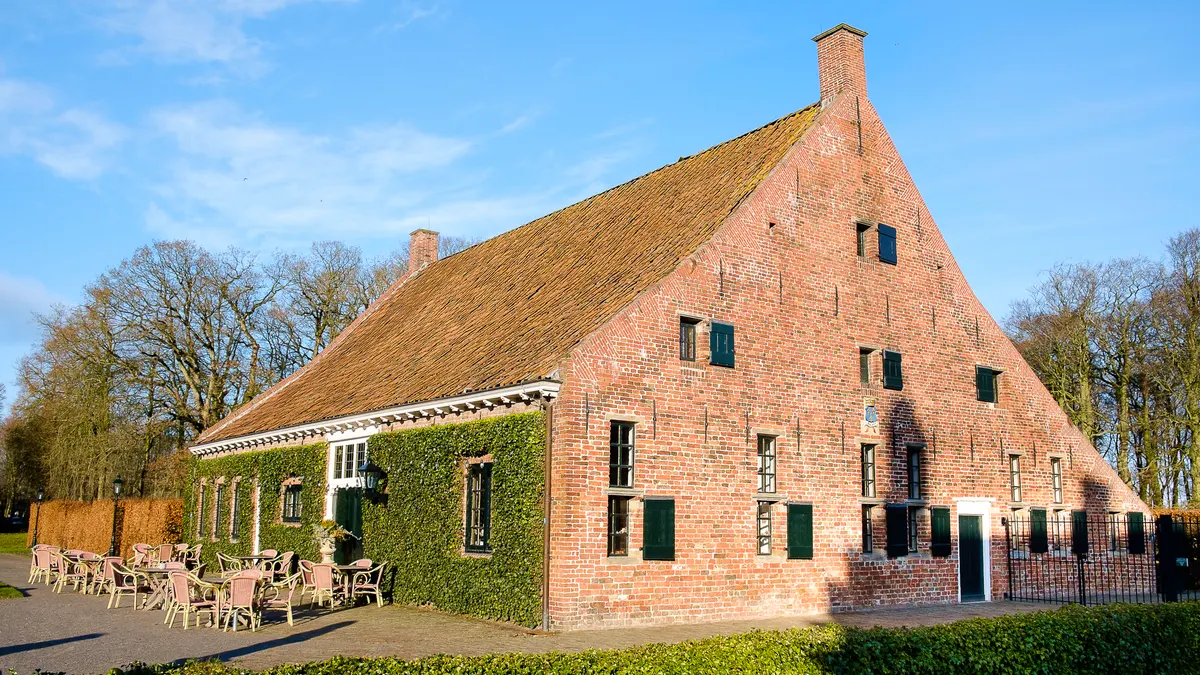 Bakstenen koetshuis met groene luiken en klimop bij een Groningse borg