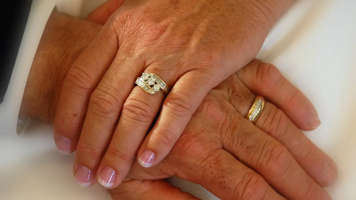 Twee oudere handen op elkaar met een verlovingsring en een gouden trouwring