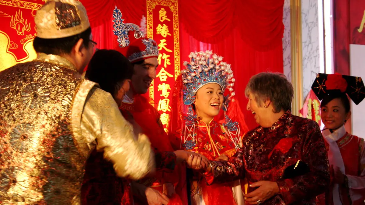 Bruid in rode Chinese trouwkledij met kroon begroet lachend de gasten