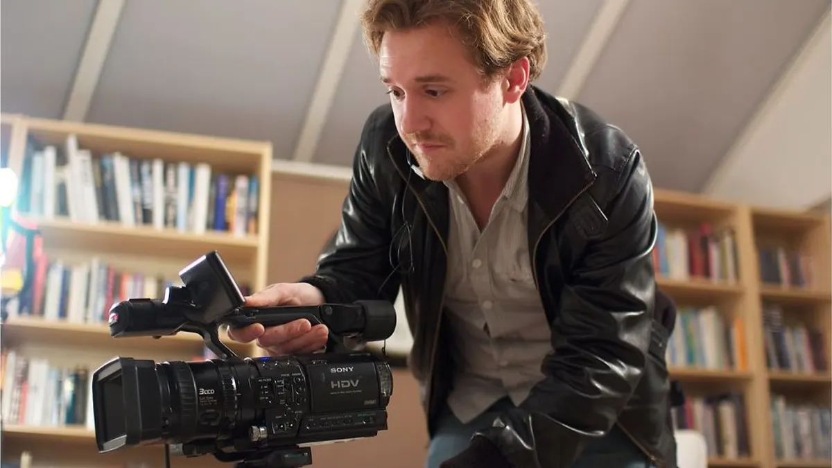 Een videograaf stelt zijn videocamera op een statief af voor een opname binnen