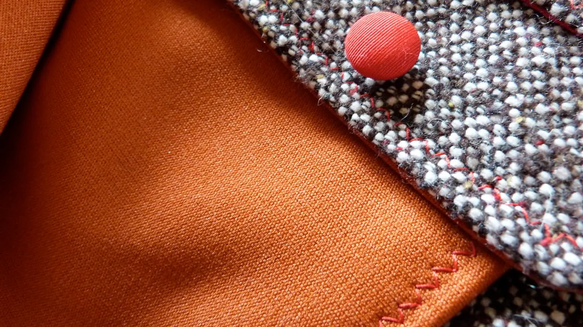 Close-up van grijze tweed met een rode stoffen knoop en een oranje voering