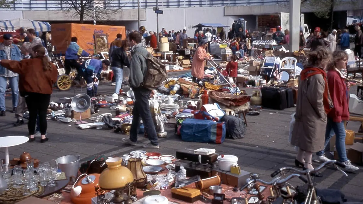 Drukke rommelmarkt met kleden en tafels vol tweedehands glaswerk, lampen en huisraad