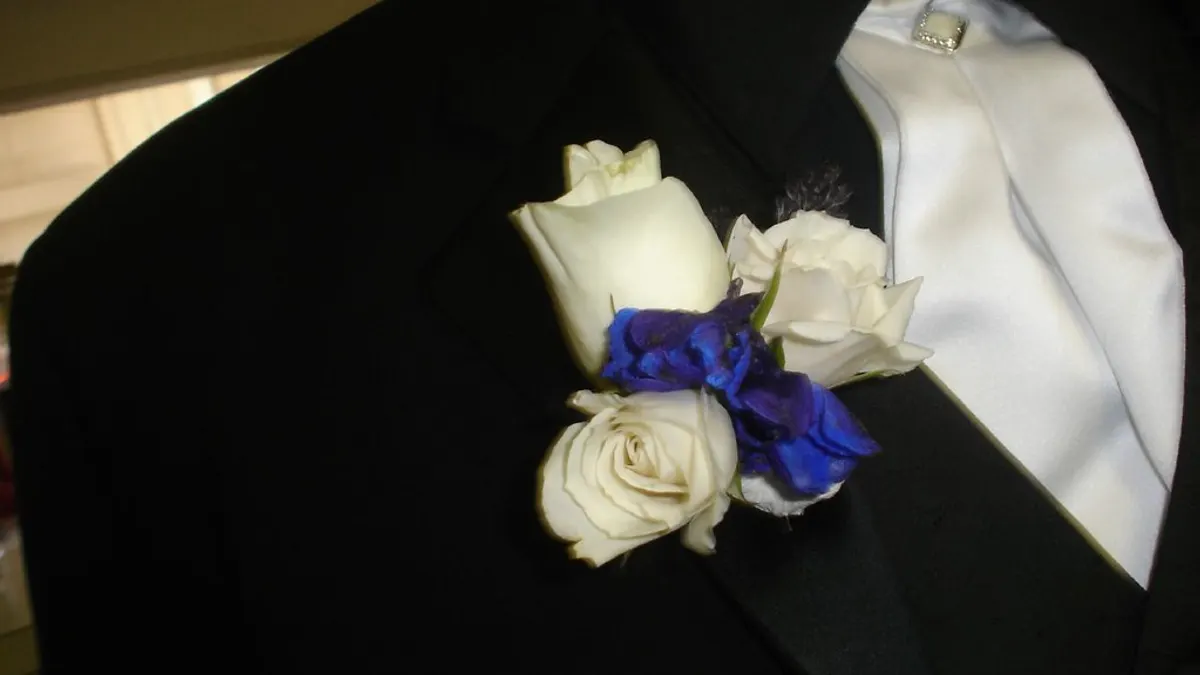 Een corsage van witte rozen en blauwe bloemen op de revers van een zwart trouwpak met witte das