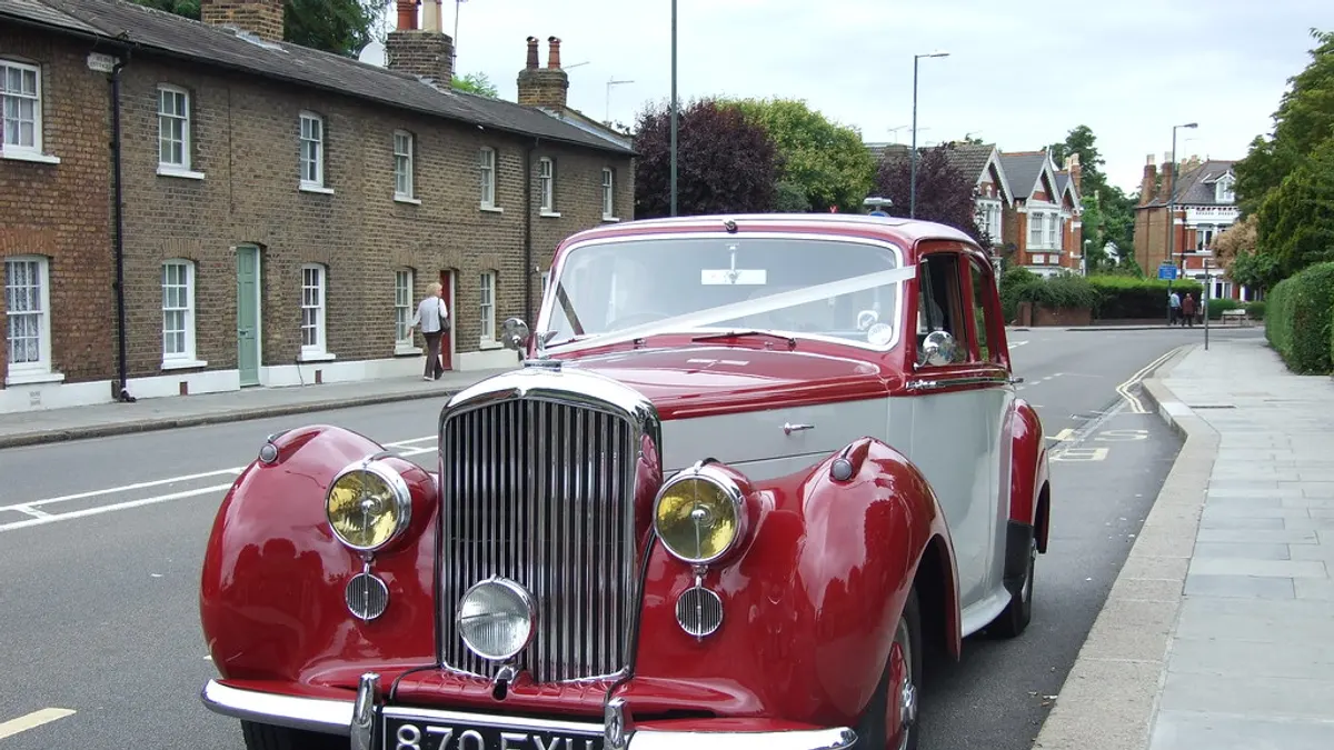 Een rode oldtimer met wit lint staat geparkeerd in een straat met rijhuizen
