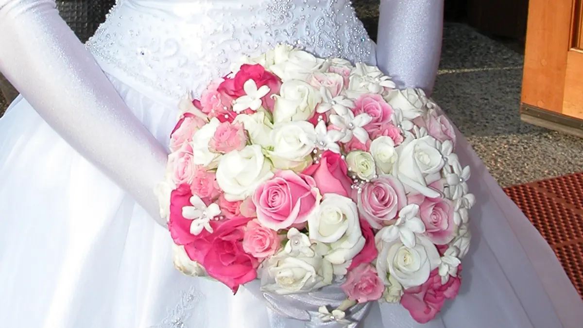 Bruid houdt een rond bruidsboeket met witte en roze rozen vast