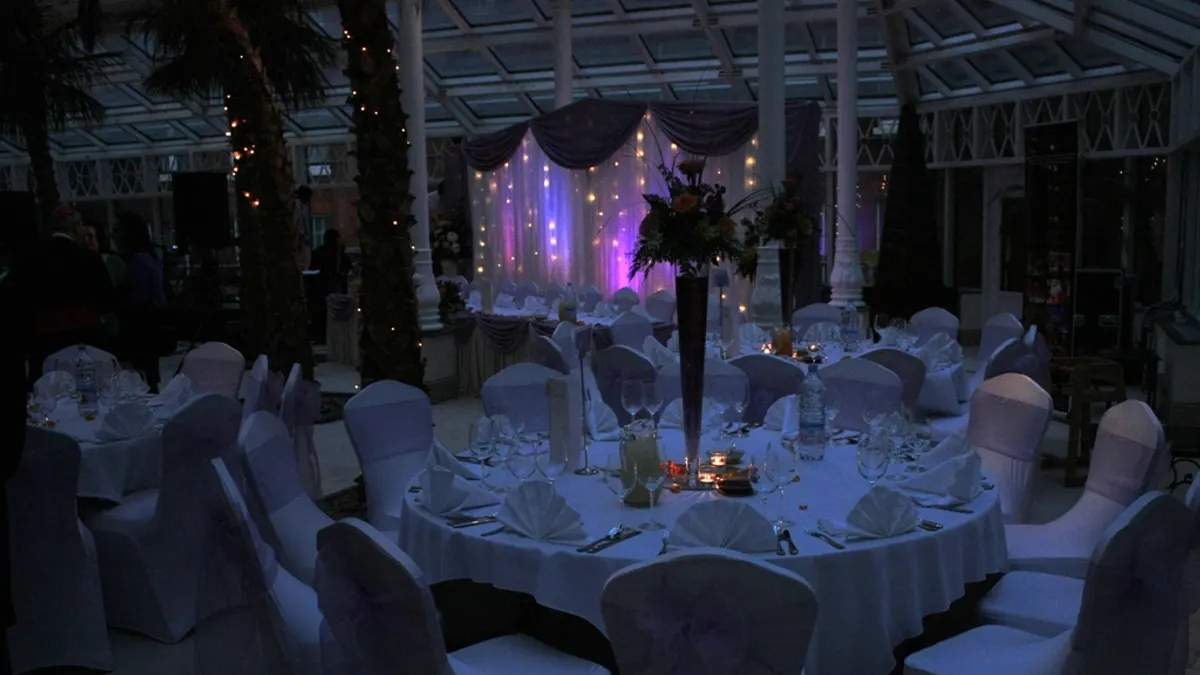 Een feestzaal met ronde tafels, witte stoelhoezen en paarse sfeerverlichting