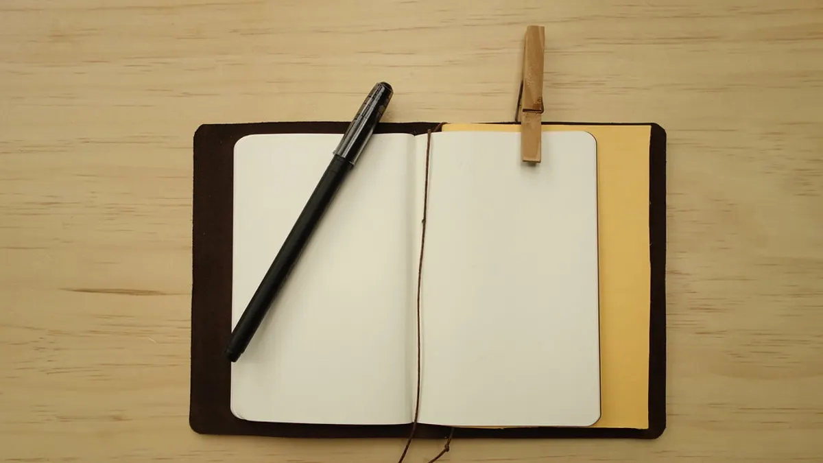 Open notitieboekje met lege bladzijden en een zwarte pen op een houten tafel