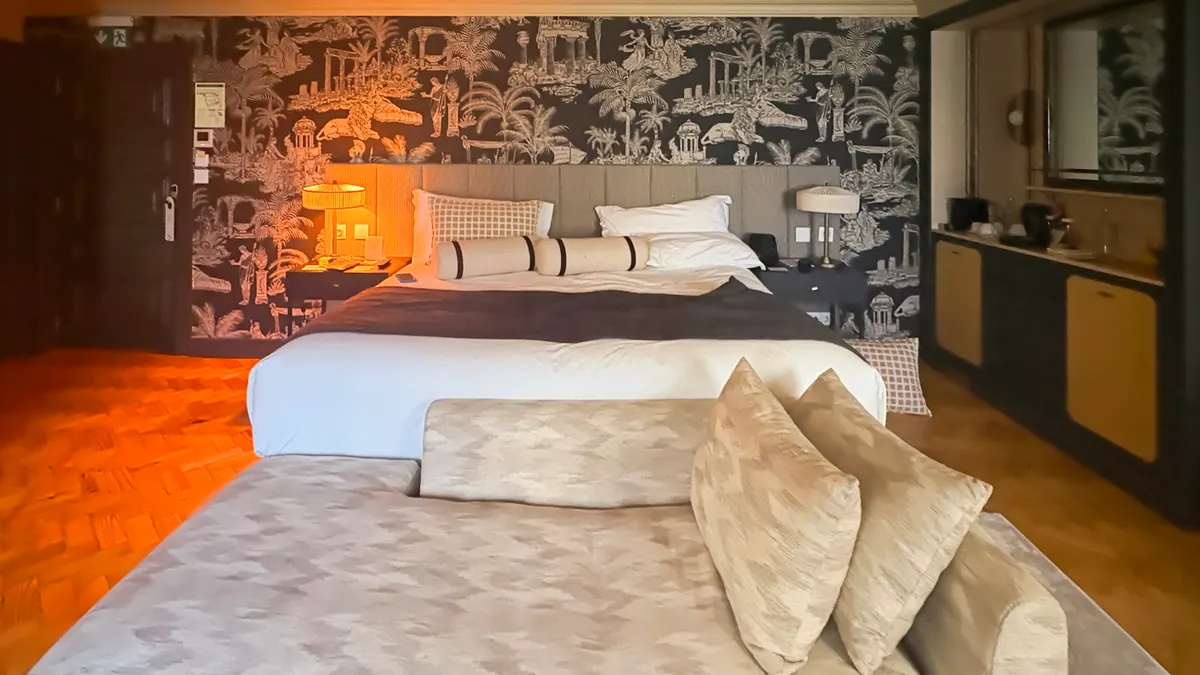 Een sfeervolle hotelkamer met een opgemaakt tweepersoonsbed, zachte lampen en behang met palmmotief