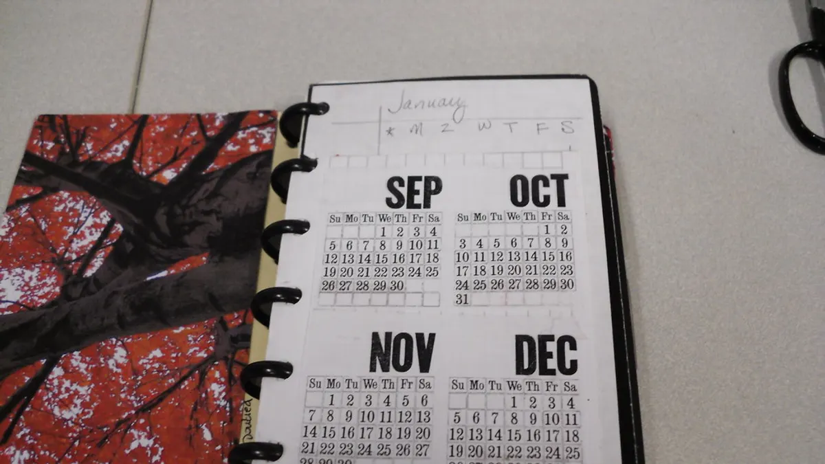 Een opengeslagen agenda met een jaaroverzicht van september tot december naast een kaft met een herfstboom