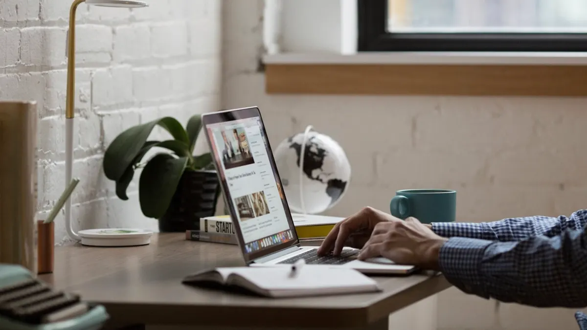 Bureau bij het raam met een laptop en een notitieboekje, waar de teksten voor de trouwwebsite worden uitgeschreven