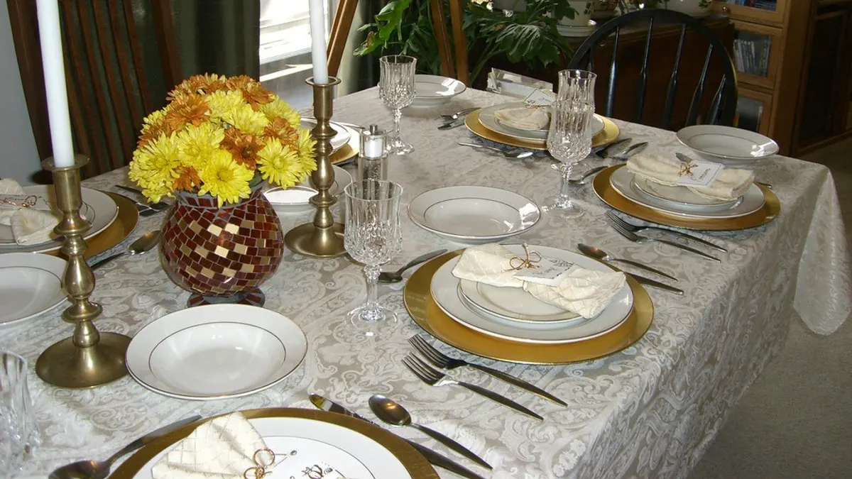 Feestelijk gedekte tafel met gouden onderborden, kristallen glazen, koperen kandelaars en een vaas met gele chrysanten