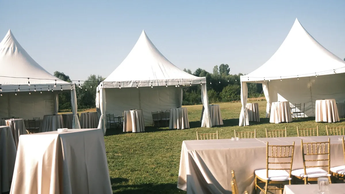 Witte feesttenten en gedekte tafels met goudkleurige stoelen staan klaar op een grasveld