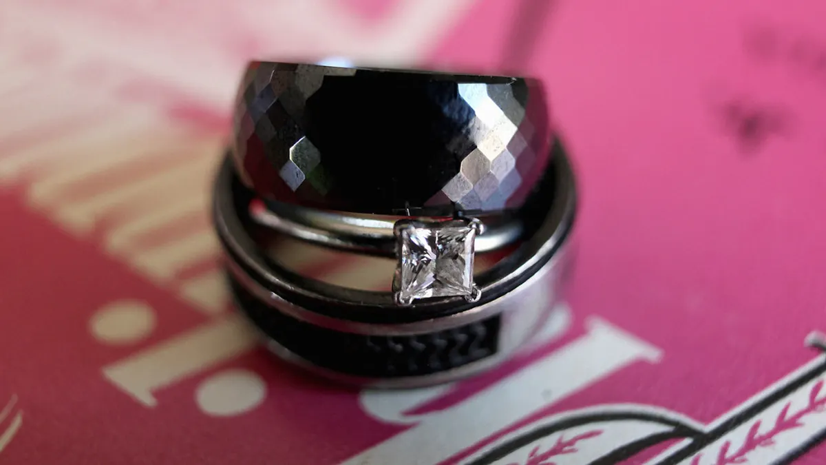 Een zwarte herenring en een verlovingsring met diamant op roze papier